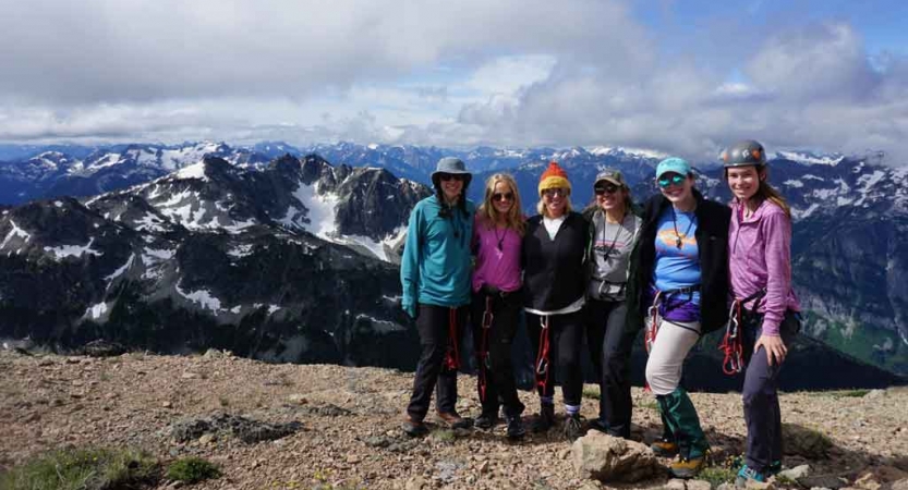 a group of women stand on a summit that overlooks a snowy mountain landscape